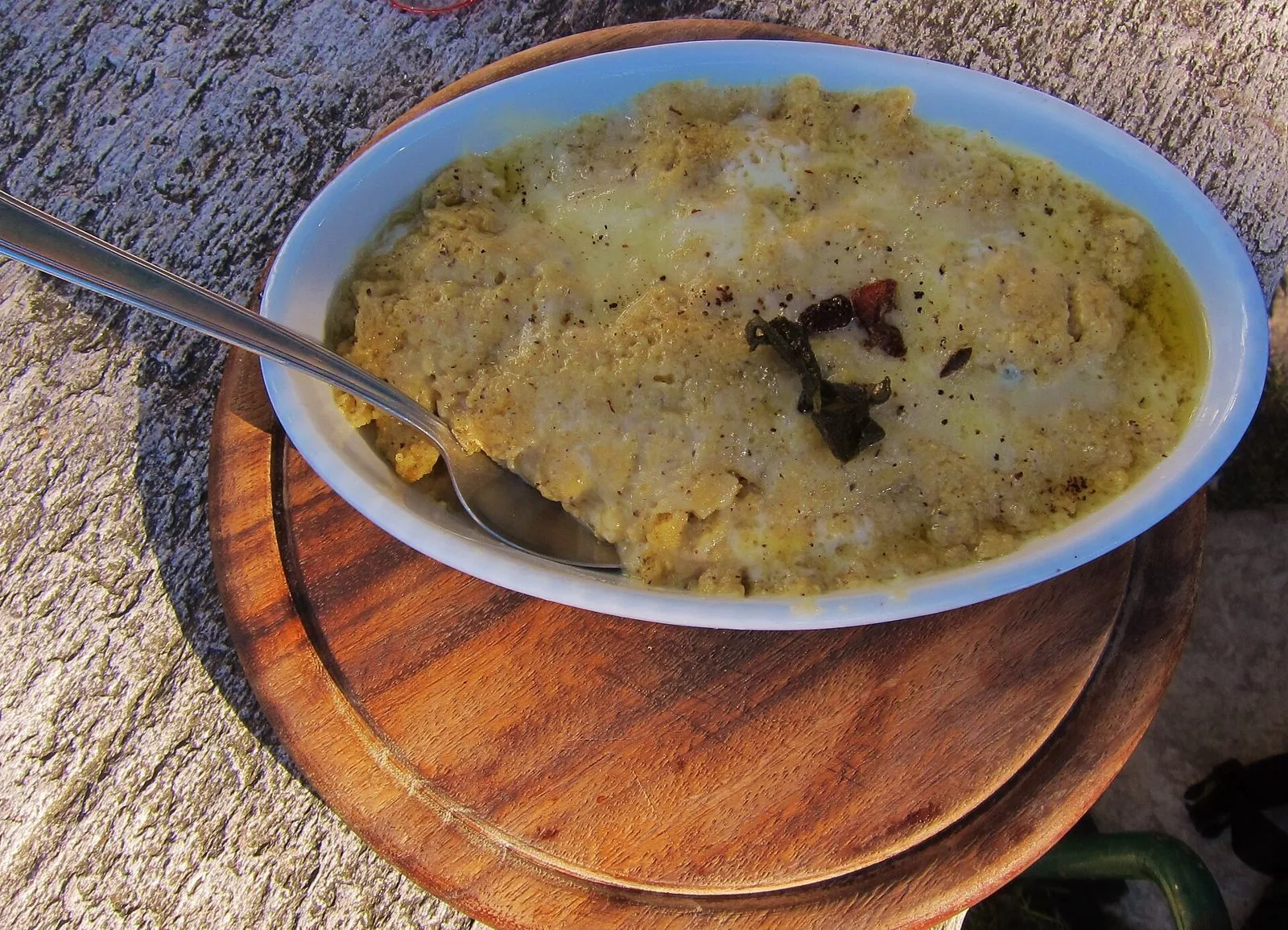 Polenta uncia con burro fuso, formaggio e salvia servita in una pirofila su un tagliere di legno